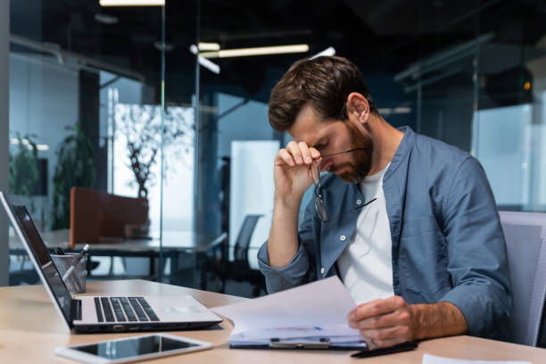 istock Upset businessman behind paper work inside modern office, mature man with beard reading financial reports and account documents unhappy with results and disappointed with achievements 1450770266