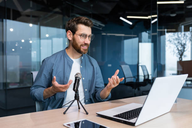 istock Business coach inside office recording audio podcast, businessman working at laptop using professional microphone and laptop for online radio, and training Remote 1450770375