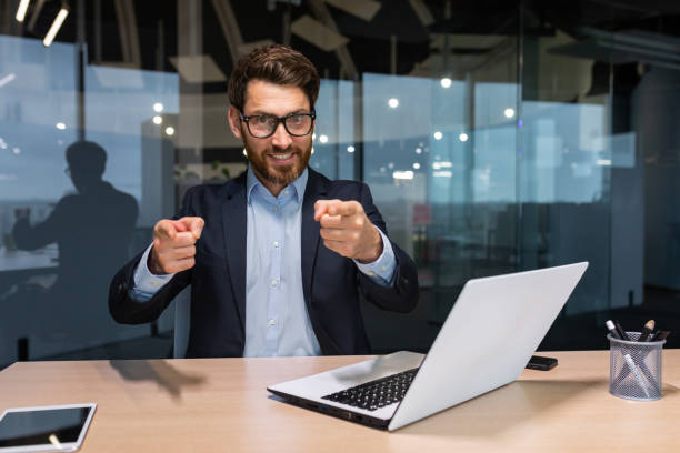 istock Successful mature businessman looking at camera and pointing finger forward calling to action, investor in business suit inside modern office working on laptop, boss with beard and glasses 1450770547