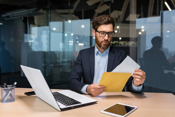 istock Mature and serious businessman inside office thoughtfully reading letter received notification, man in business suit investor at work using laptop 1450770664