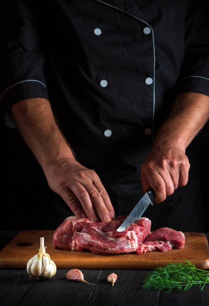 プロのシェフがキッチンでナイフで肉をカットし、料理を準備します。レストランのキッチンテーブルに野菜やスパイスを載せて、おいしいランチをご用意します。 - veal meat raw steak ストックフォトと画像