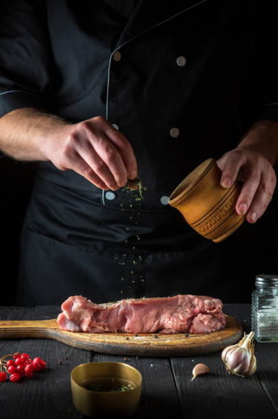 un chef professionnel prépare de la viande de veau crue. avant la cuisson, le chef ajoute un assaisonnement sec à base de plantes au bœuf. le plat national est préparé dans la cuisine du restaurant - veal calf meat baking photos et images de collection