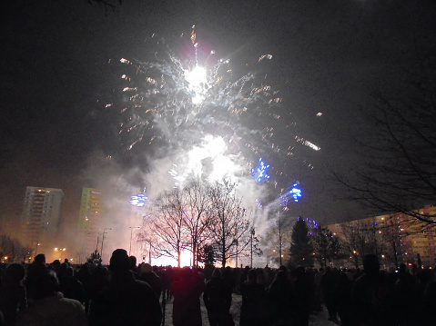 Smoking effect of white fireworks during New Year pyrotechnics show flashing on buildings and people.