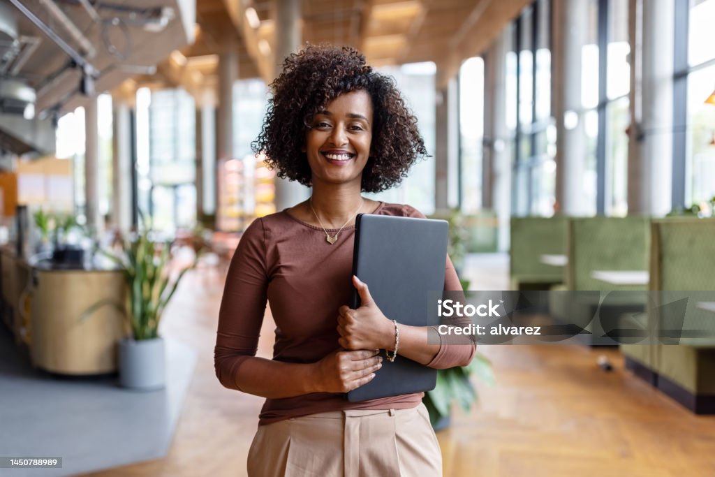 Portrait of happy African businesswoman holding digital tablet in the office Portrait of happy African businesswoman holding digital tablet standing in the office. Female entrepreneur at her startup office looking at camera and smiling. Women Stock Photo