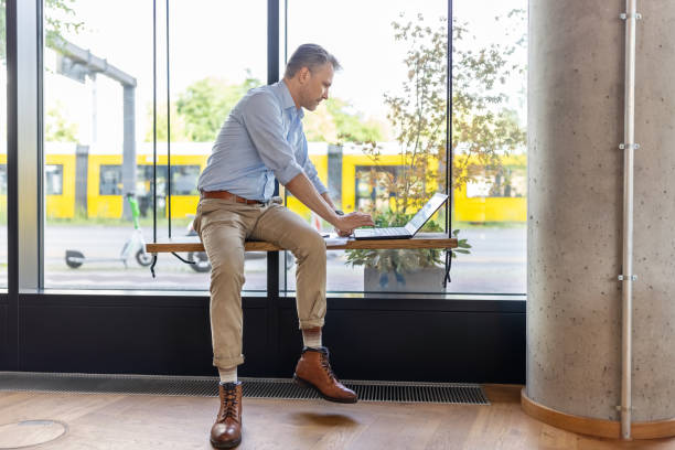 istock Businessman using laptop sitting on swing at office lobby 1450789004