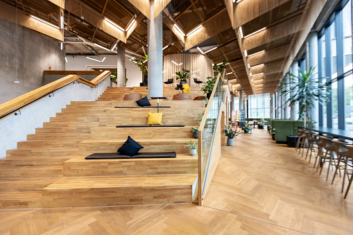 Innovative office with workstations on wooden staircase and restaurant in the background. Brightly lit modern and spacious office interior.