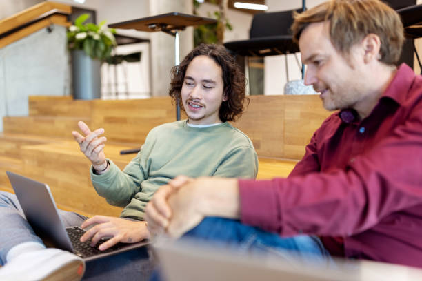 Young man talking with colleague looking at laptop in creative office