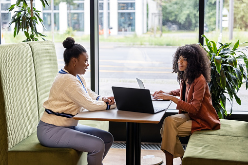 Side view of two businesswomen discussing work sitting at a restaurant. Female entrepreneur talking with a business partner at coffee shop.