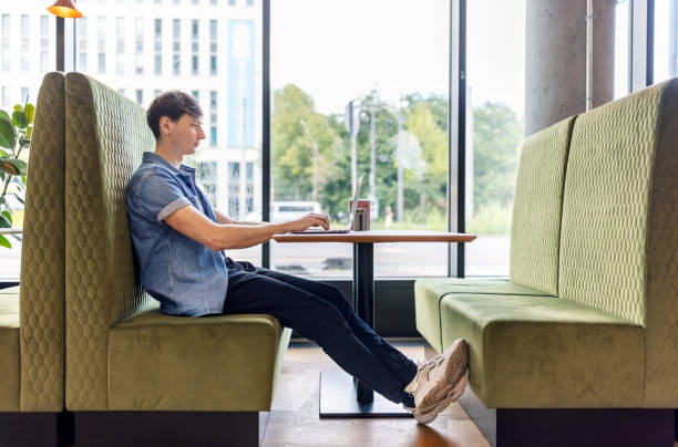 Side view of a young man sitting at a restaurant working on laptop. Man in casuals using laptop sitting at cafe.