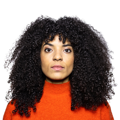 Serious looking woman photographed in the studio. Young female with curly hair against white background.