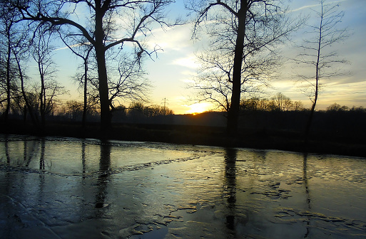 Beautiful sunset at partially frozen pond during snowless winter.