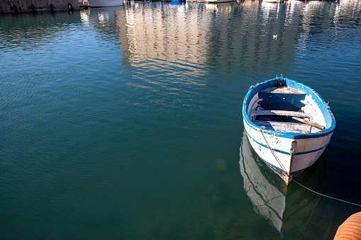 Fishing boat on the water in Ortigia island with the cityscape reflection of Syracuse in Sicily, Italy