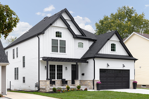 Barrington, IL, USA - October 5, 2021: A traditional modern farmhouse with white siding, black roof and garage door, and a covered front porch.