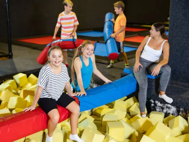 Photo of Cheerful teen sisters spending time in pool with foam cubes