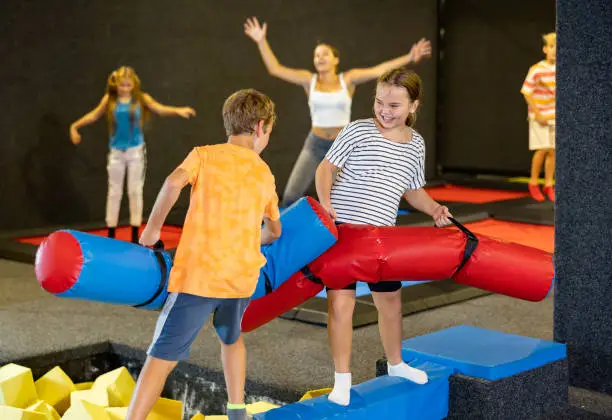 Photo of Preteen girl fighting by pugil stick with boy on inflatable beam