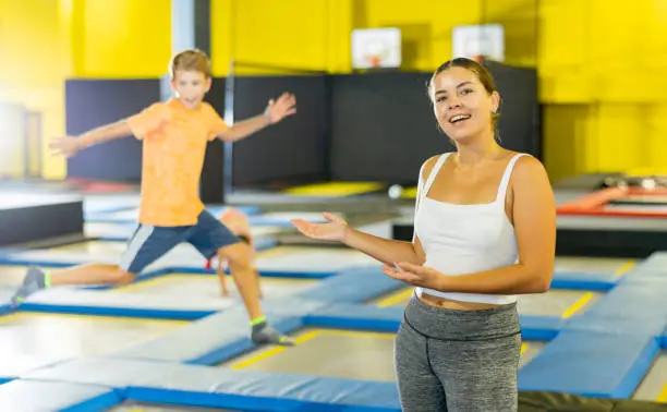 Photo of Teacher with children in trampoline center against background of children playing and jumping on trampoline
