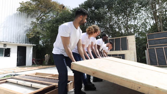 Group of Latin American volunteers working as a team while building a house placing a panel at the side of the house