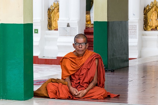 11/07/2019 Shwedagonm pagoda, Yangon, Myanmar\nSenior monk in orange traditional buddhist dress walking inside the temple on white marble floor