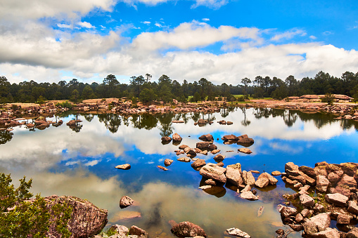Rocas en un lago, reflejo del cielo en el agua, nubes blancas en un cielo azul, bosque y rocas grandes alrededor, parque natural mexiquillo en Durango, sierra madre occidental