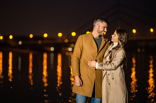 Beautiful young couple embracing next to river shore at night on autumn day.