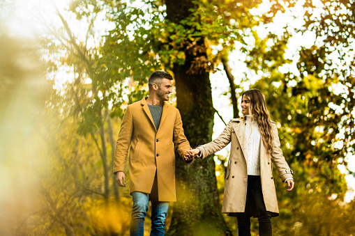 Beautiful young couple walking and holding hands in autumn park.
