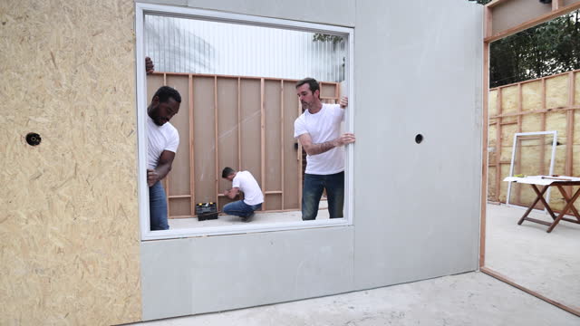 Volunteers installing window frames at a construction site while others work at background