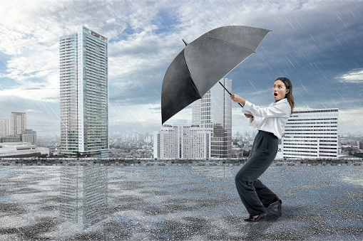 Asian businesswoman holding a black umbrella because of rain in the city