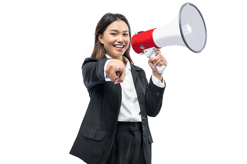 Asian businesswoman talking on a megaphone and pointing to the camera isolated over white background