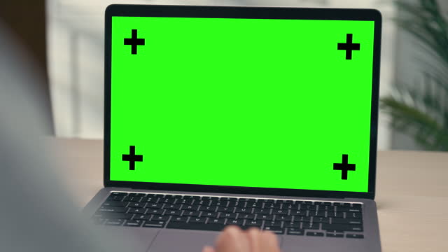 Closeup of young Asian woman using laptop with mock-up green screen while working in living room at home. Chroma key technology, Marketing design.