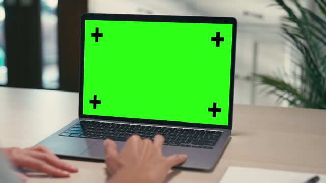 Closeup of young Asian woman using laptop with mock-up green screen while working in living room at home. Chroma key technology, Marketing design.