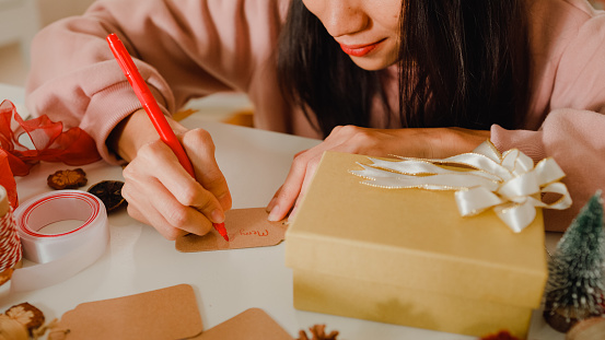 Closeup of woman hands writing greeting card with christmas gift boxes on table at home. New Year and Christmas concept.