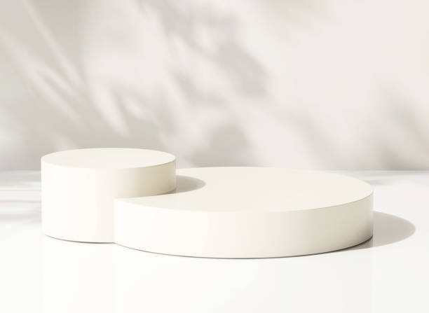 Two glossy cream round cylinder ceramic podium on white table counter in dappled sunlight and leaf shadow on white wall background