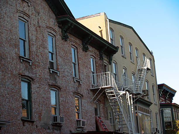 This quaint 20th century brick apartment building with fire escape is in the small town of Lambertville, New Jersey, near the Delaware River. The reflective late afternoon lighting gives a blue glow to the windows. Image was created on a DSLR at low ISO and depicts a piece of Americana from an earlier time. Copy space in right corner.     