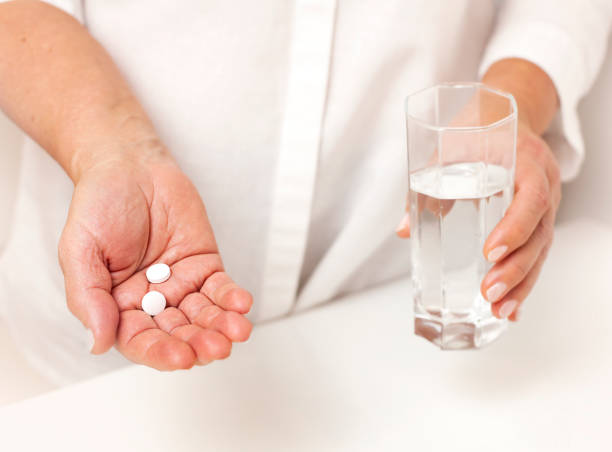 istock hand with pills and glass of water on white table 1450920077