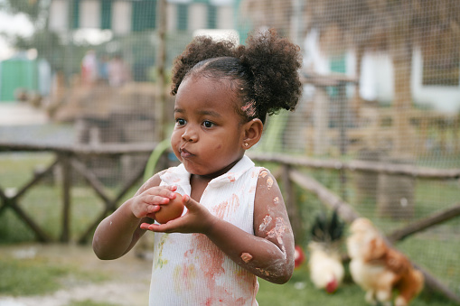 African-American child holding chicken egg with color stain on hand and dress.