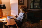 Woman working on laptop and smartphone at night in the hotel room