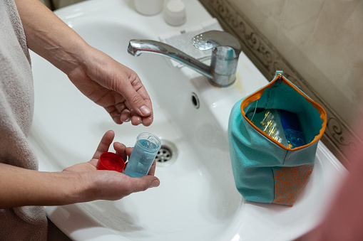 Female hands take estrogen gel from the package. The woman stands in front of the bathroom sink wrapped in a towel after taking a shower.