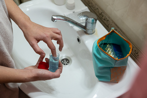 Female hands take estrogen gel from the package. The woman stands in front of the bathroom sink wrapped in a towel after taking a shower.