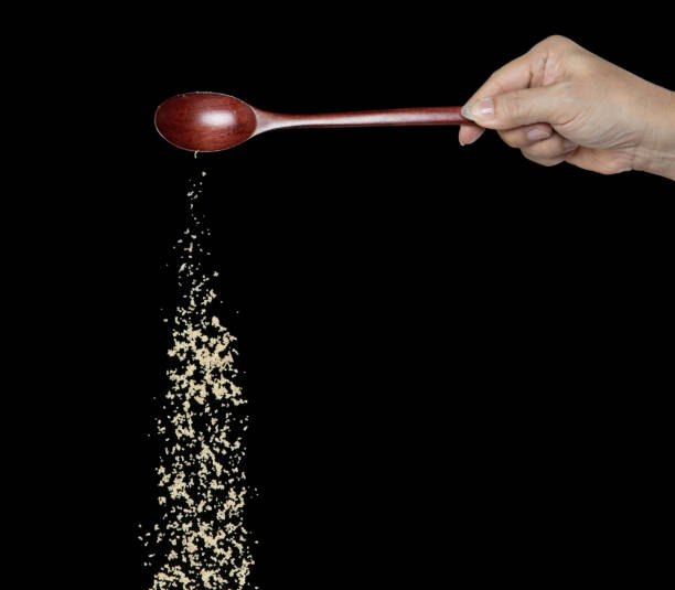 istock Brown Sugar fall, brown grain sugar pouring down abstract cloud fly from wooden spoon. Beautiful complete seed sugarcane, food object design. Selective focus freeze shot Black background isolated 1450926632