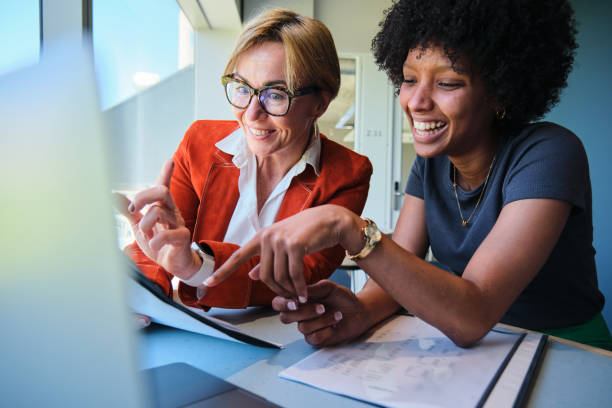istock Businesswomen laughing together while going over paperwork at an office desk 1450932847