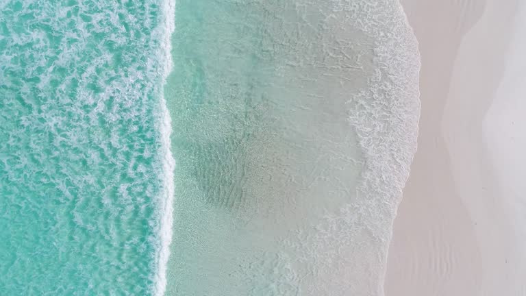 Fixed shot directly above gentle waves lapping on a pristine white sand beach and turquoise water