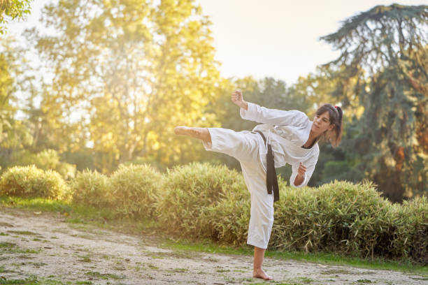 combattante de karaté avec ceinture noire pratiquant la pose de coup de pied à l’extérieur dans la nature. - martial arts women tae kwon do black belt photos et images de collection