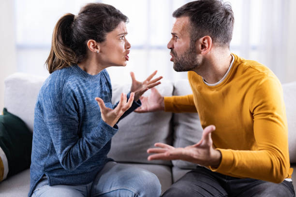 Mid adult couple arguing on sofa at home. Frustrated couple having a fight during their relationship breakup at home. arguing stock pictures, royalty-free photos & images