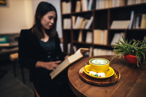 Middle-aged businesswoman sitting and reading a book at Book Café, enjoying hot Matcha latte. Hoan Kiem, Hanoi, Vietnam