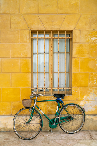 Old green bicycle leaning against yellow wall of rural Italian house