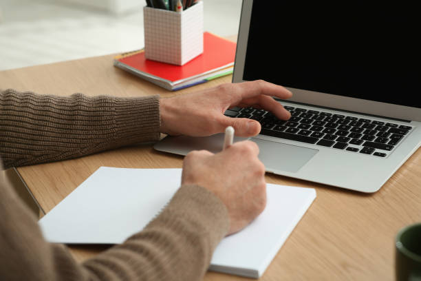 istock Man with laptop and notebook learning at wooden table indoors, closeup 1450963003