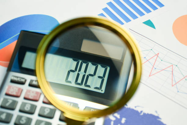 New year business and finance concept. A calculator showing 2023 on the display with magnifying glass and business finance graphs, documents on the desk stock photo
