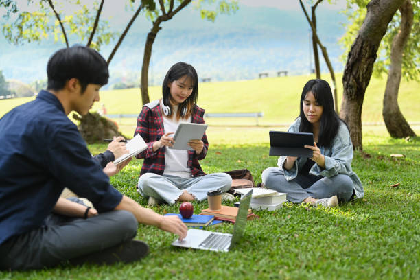 istock Group of university students working and reading book while sitting together on green lawn at university campus. 1450965985