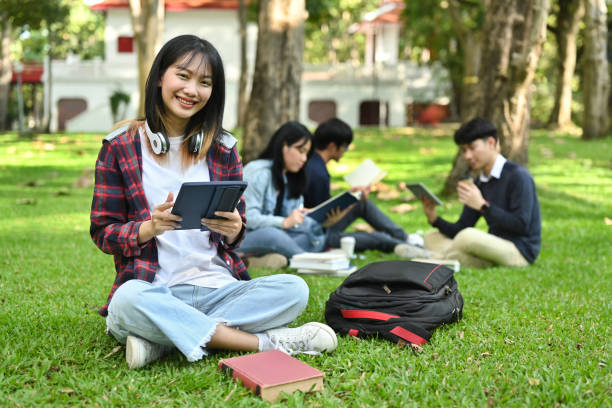 istock Cheerful asian female college or university student using digital tablet on green grass in the campus. 1450966065