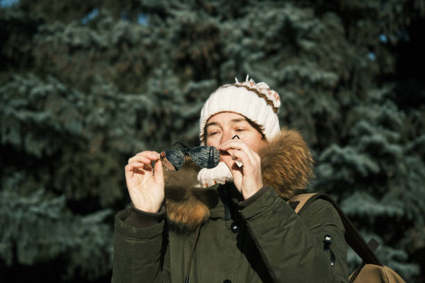 Winter day, happy smiling young woman with snowflakes toys having fun enjoys snow, warm weather against Christmas tree, joyful girl in hat standing in snowy forest